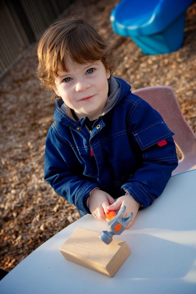 Child holding a toy hammer over a block of wood