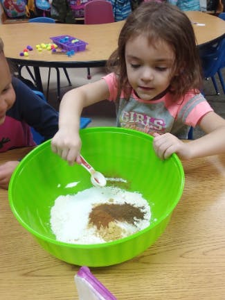 Child mixing ingredients in a green bowl with a spoon