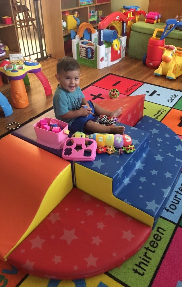 Child sitting on a play mat surrounded by toys