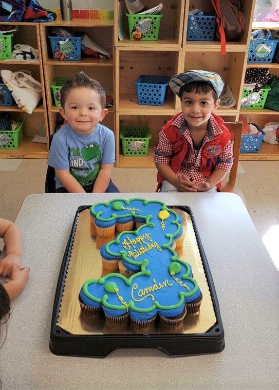 Two children sitting at a table with a number 3 cupcake cake