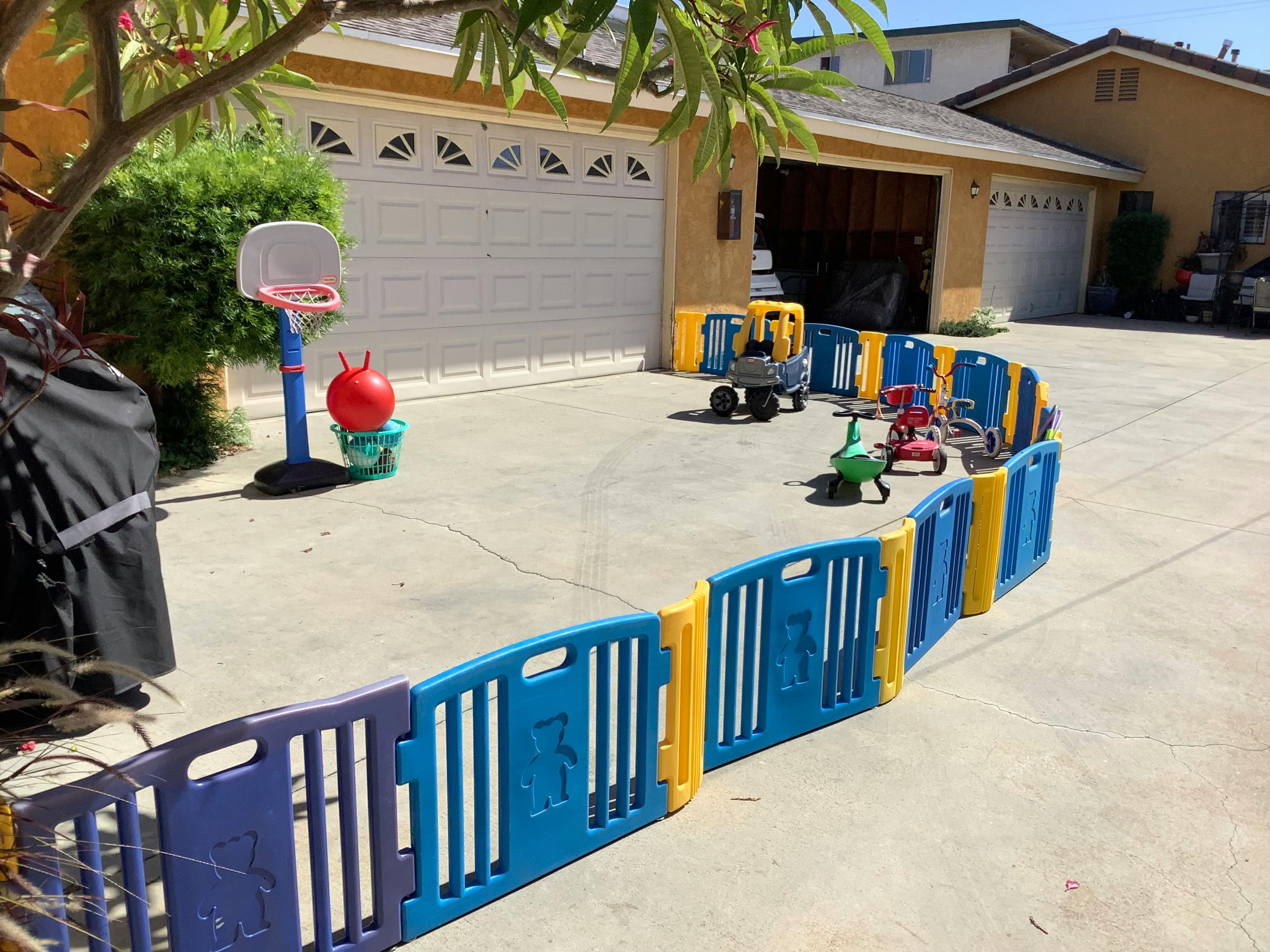 Driveway with a blue and yellow playpen, basketball hoop, and toys