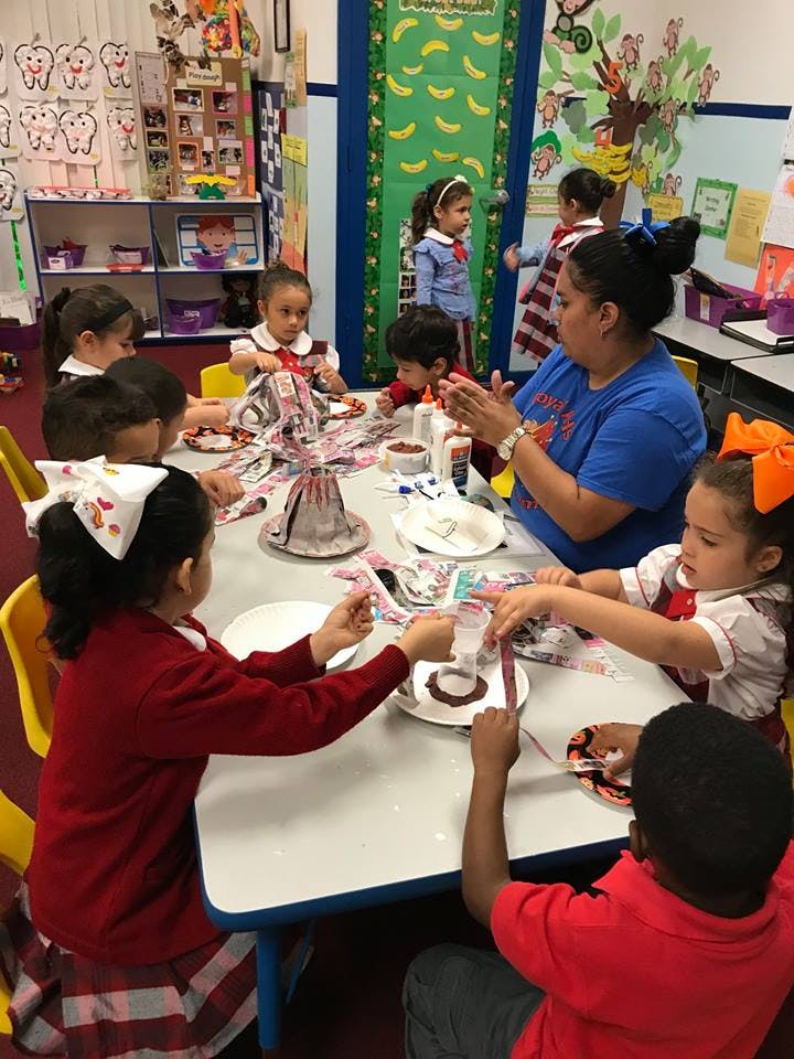 Adult and children doing crafts at a table in a classroom