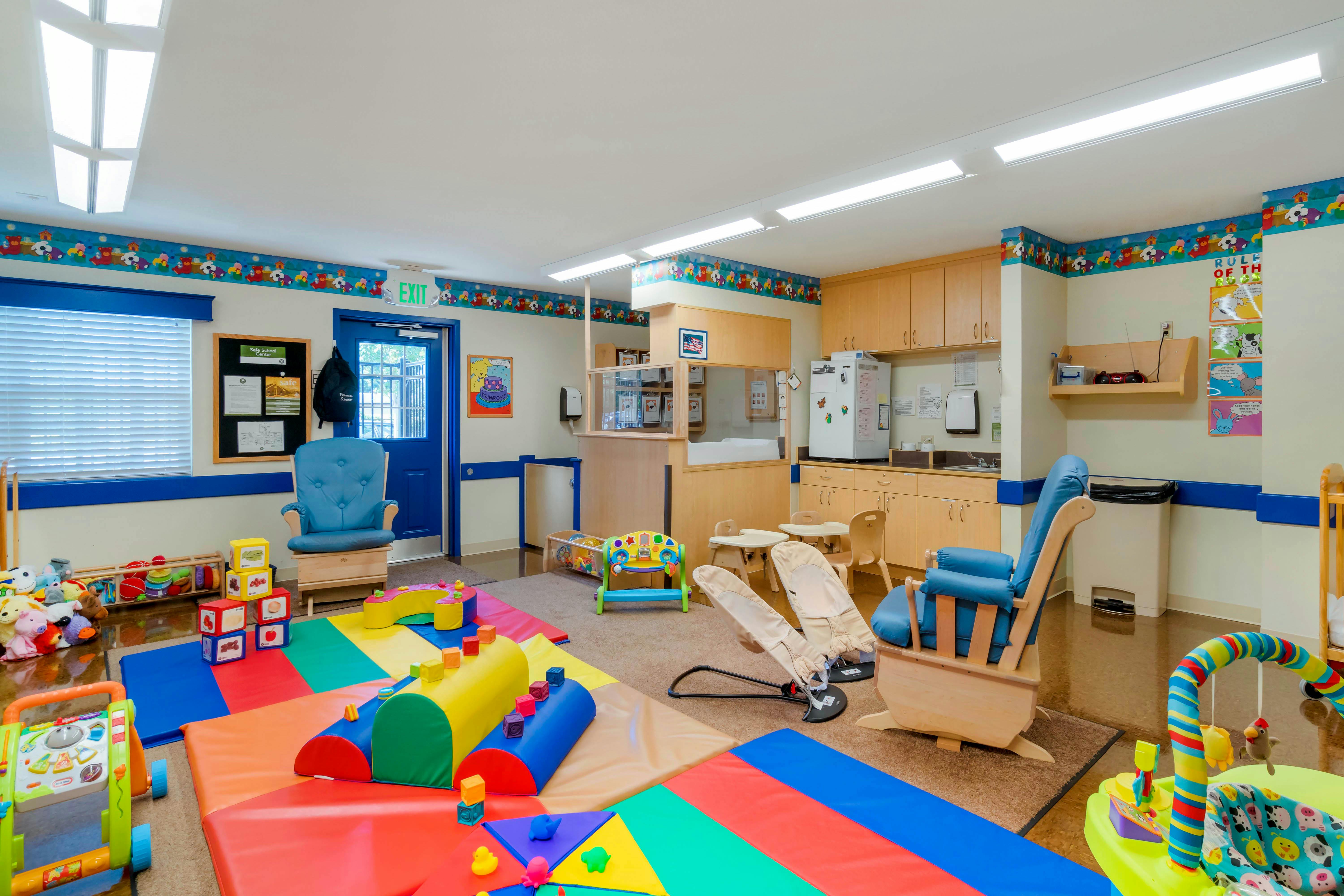 A colorful childcare classroom with toys, play mats, small tables, and chairs