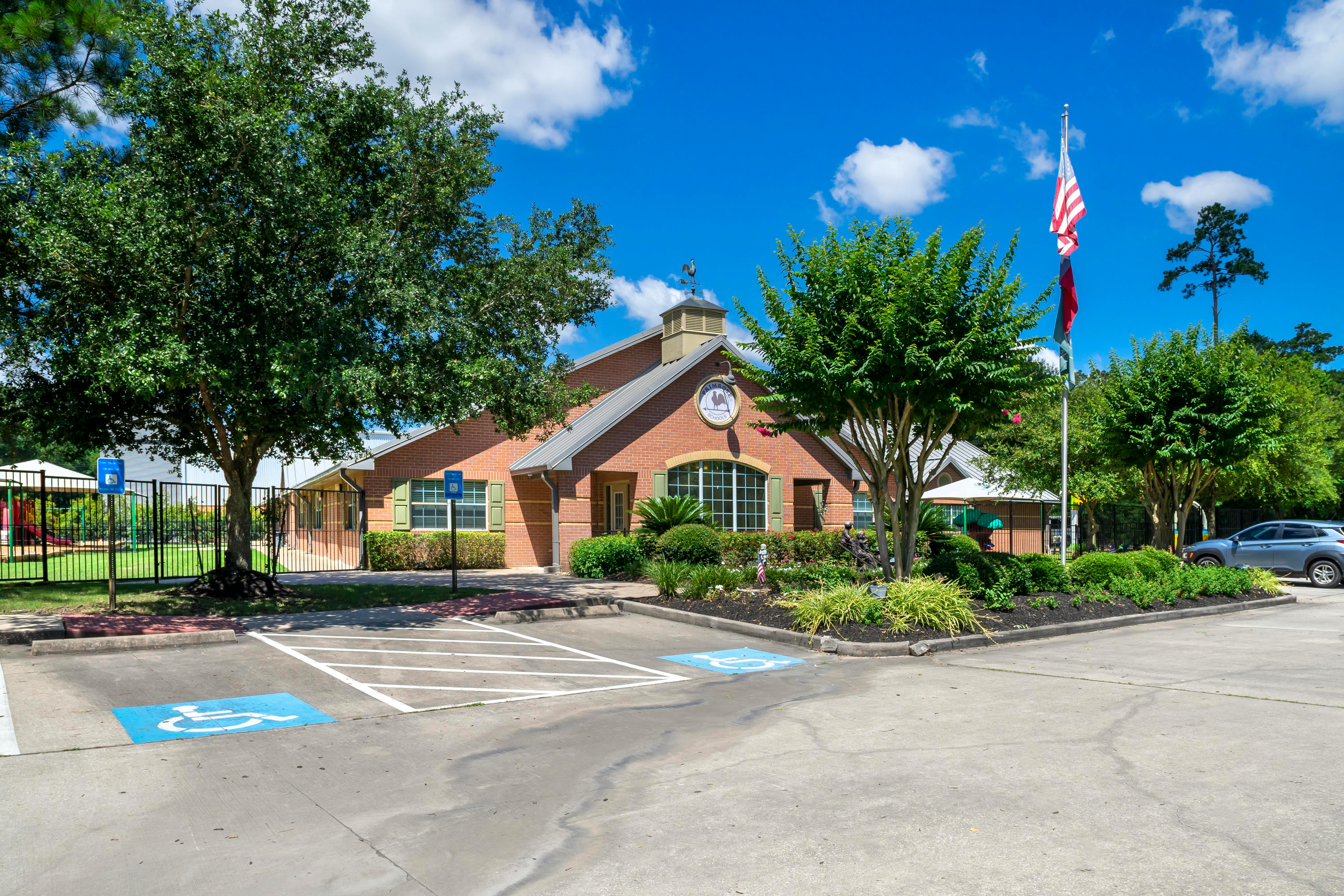 Building with brick facade and green shutters, flagpole with flags, parking lot