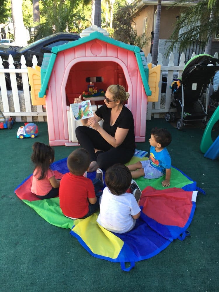 Person reading a book to three children sitting on a colorful mat outdoors