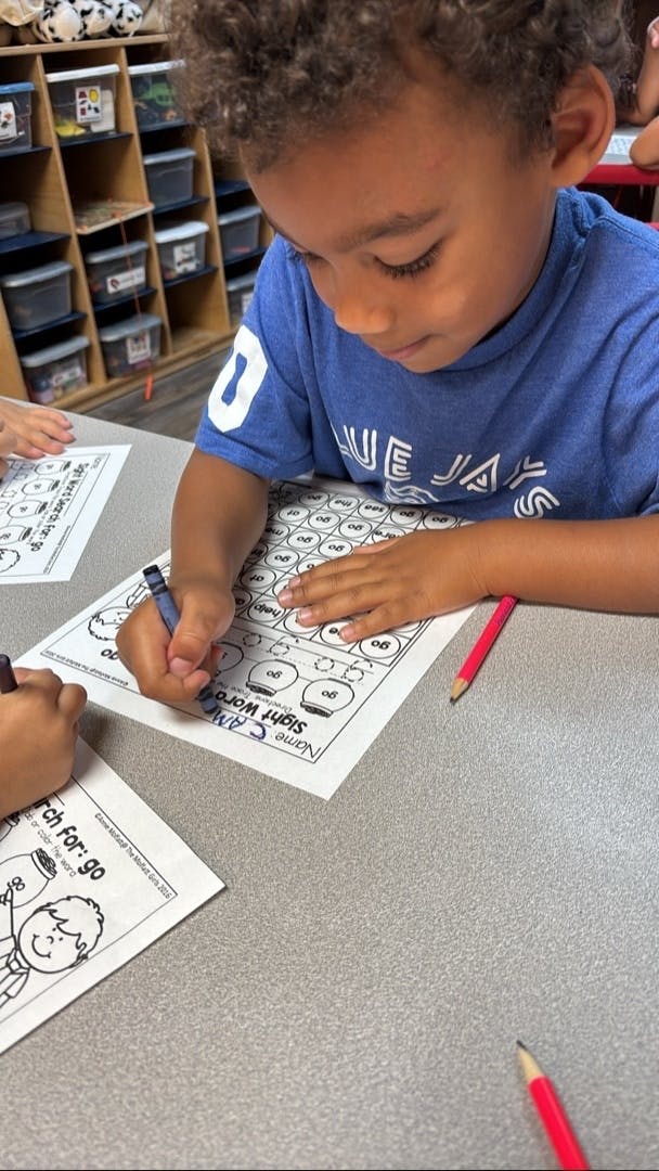 Child coloring on a worksheet at a table in a classroom