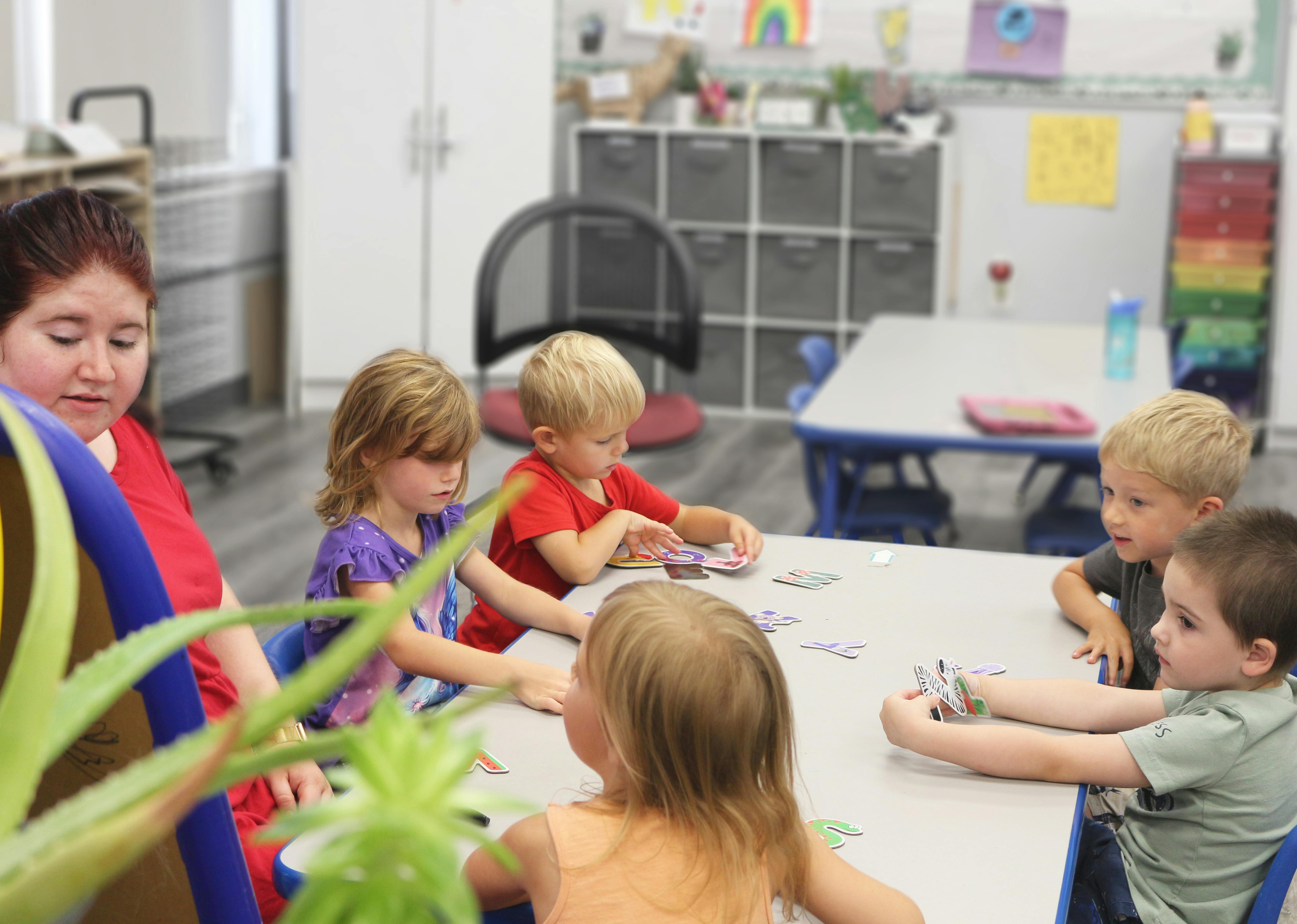 Adult and children sitting at a table playing a game in a classroom