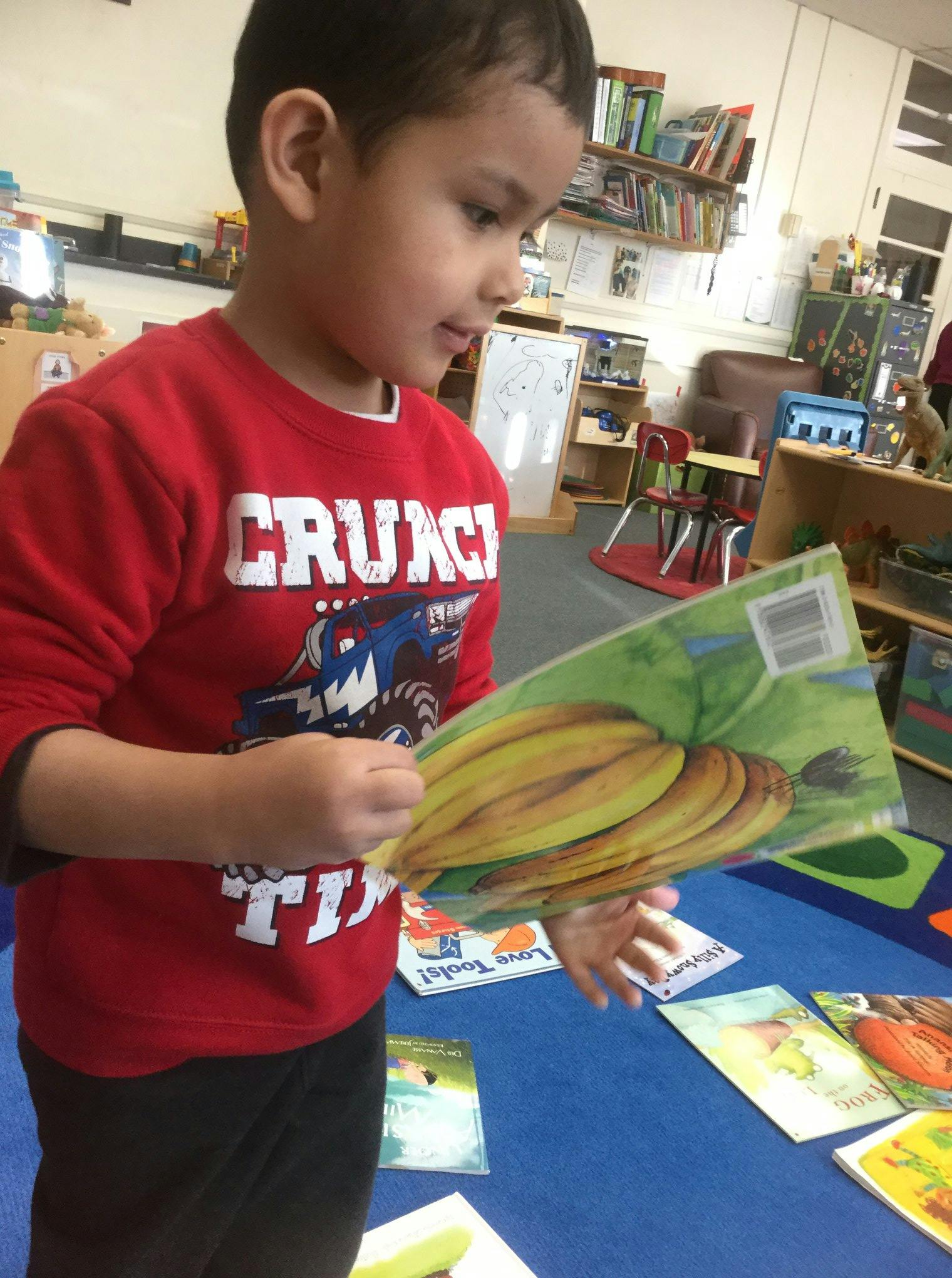 Child in a red shirt holding a book with bananas on the cover