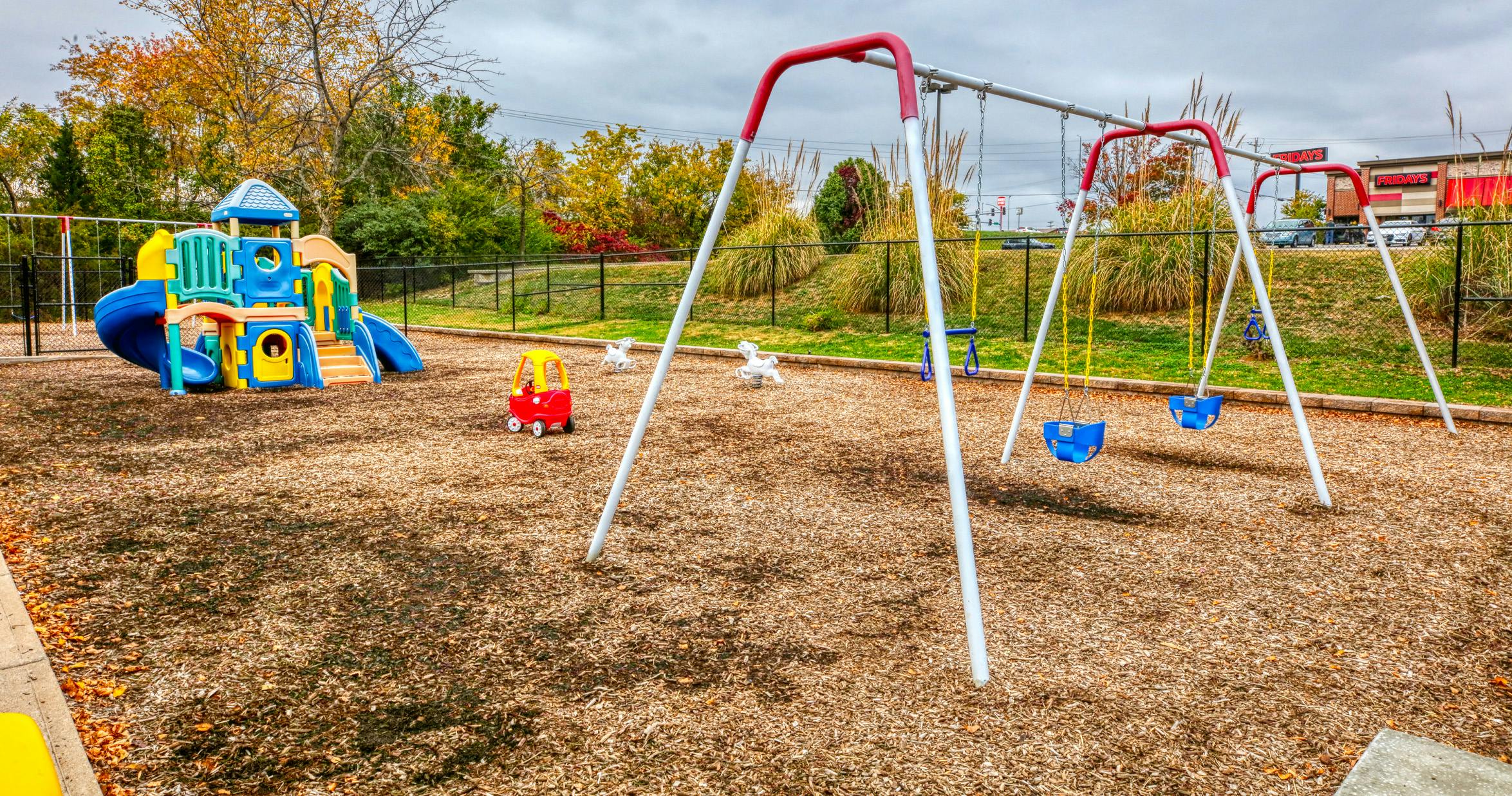 Empty outdoor playground with colorful play structure, swing set, and spring riders
