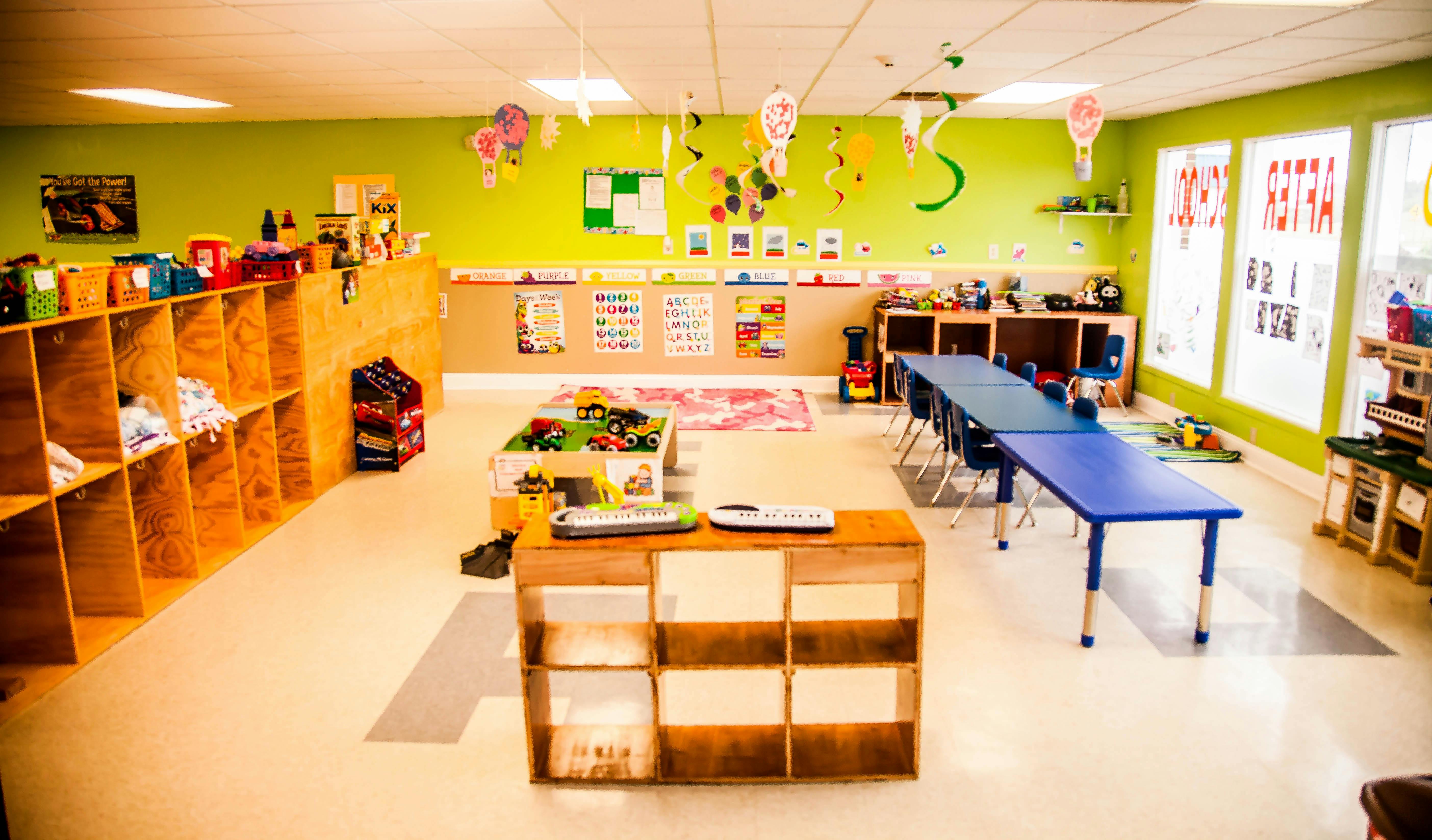Empty classroom with green walls, cubbies, and tables