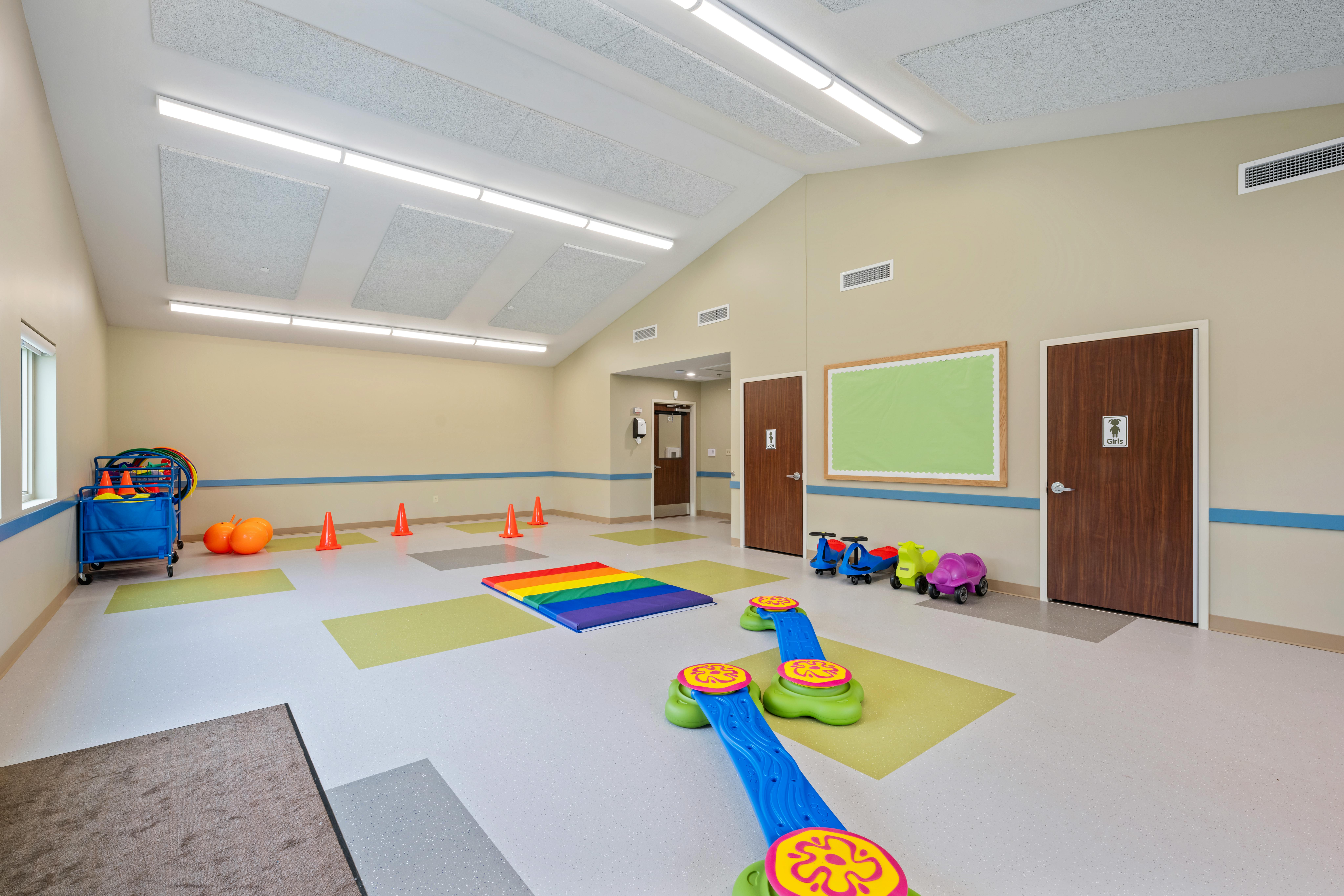 Children's play area with a rainbow mat, orange cones, and colorful ride-on toys
