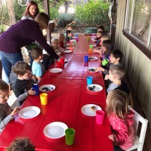 Adults serving food to children seated at a long table