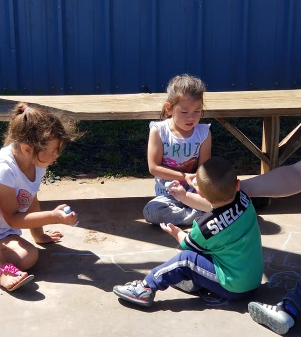 Three children sitting on the ground playing with small objects