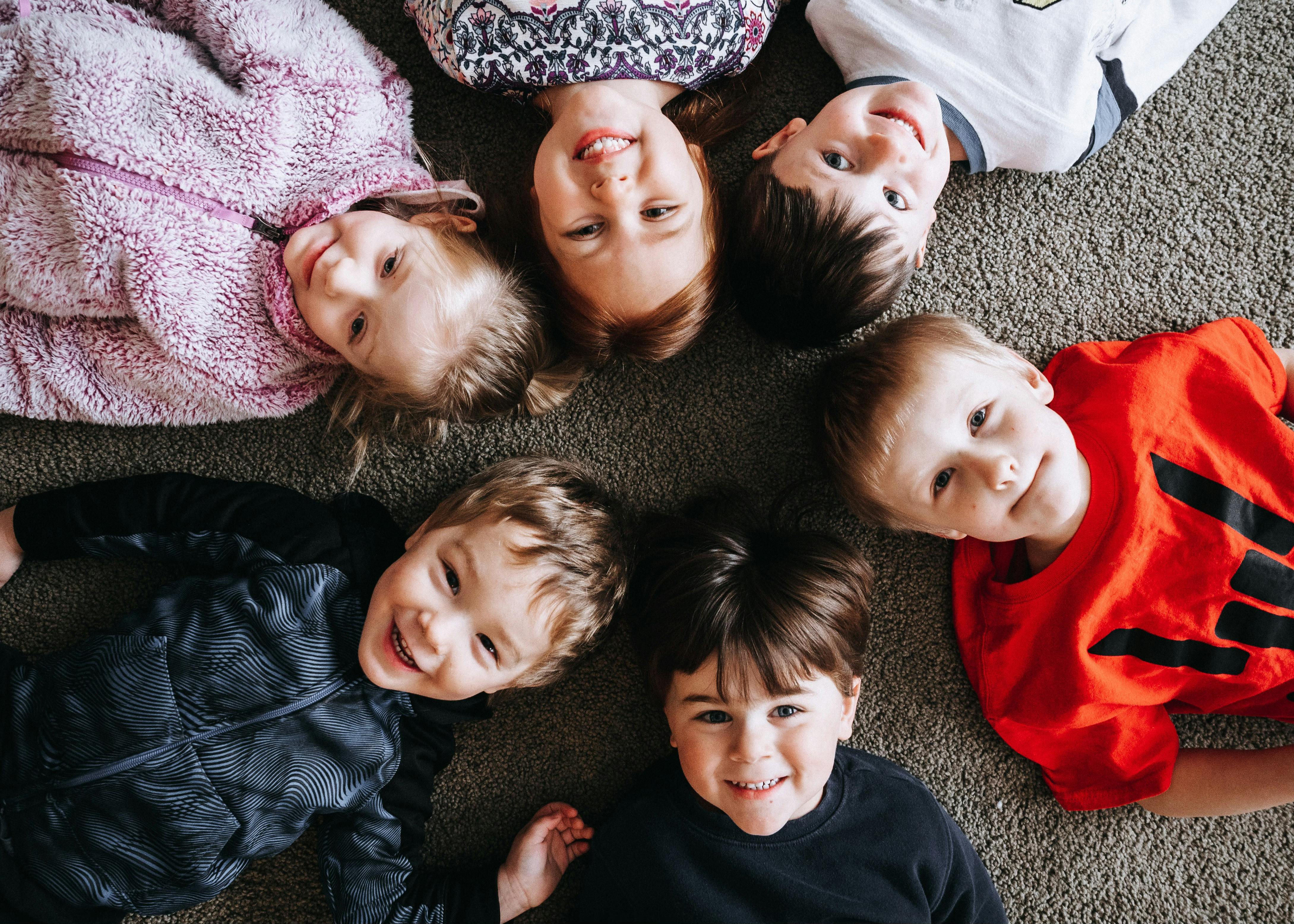 Six children lying on the floor in a circle, looking up