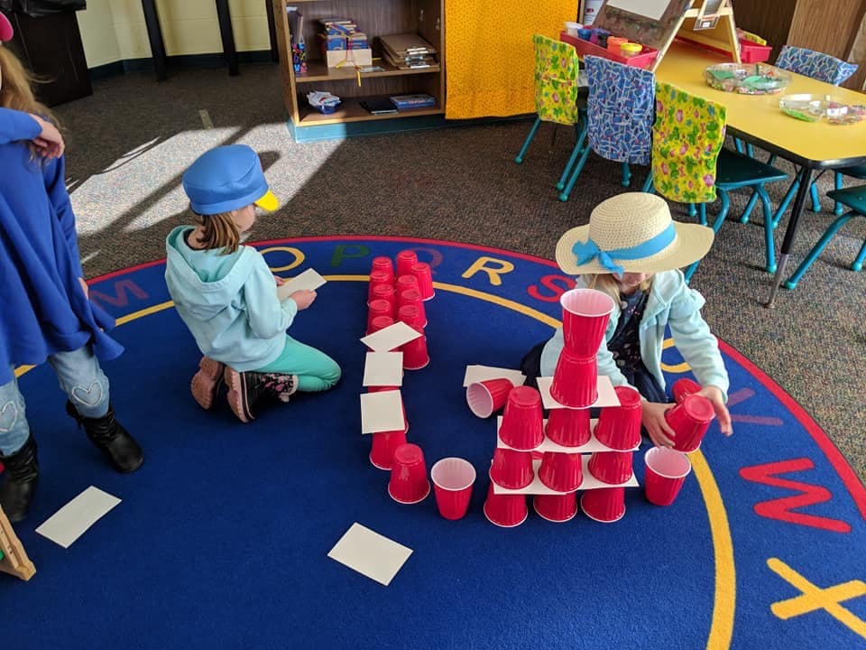 Children playing with red cups and white cards on a blue rug