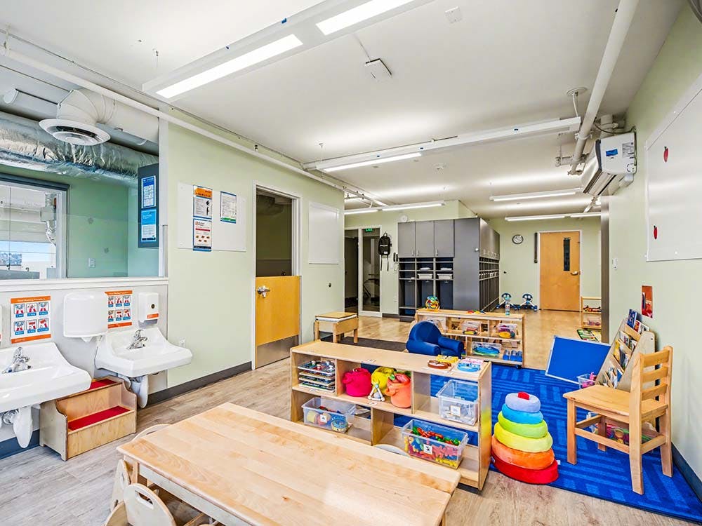 Classroom with small tables, chairs, two sinks, and shelves of toys