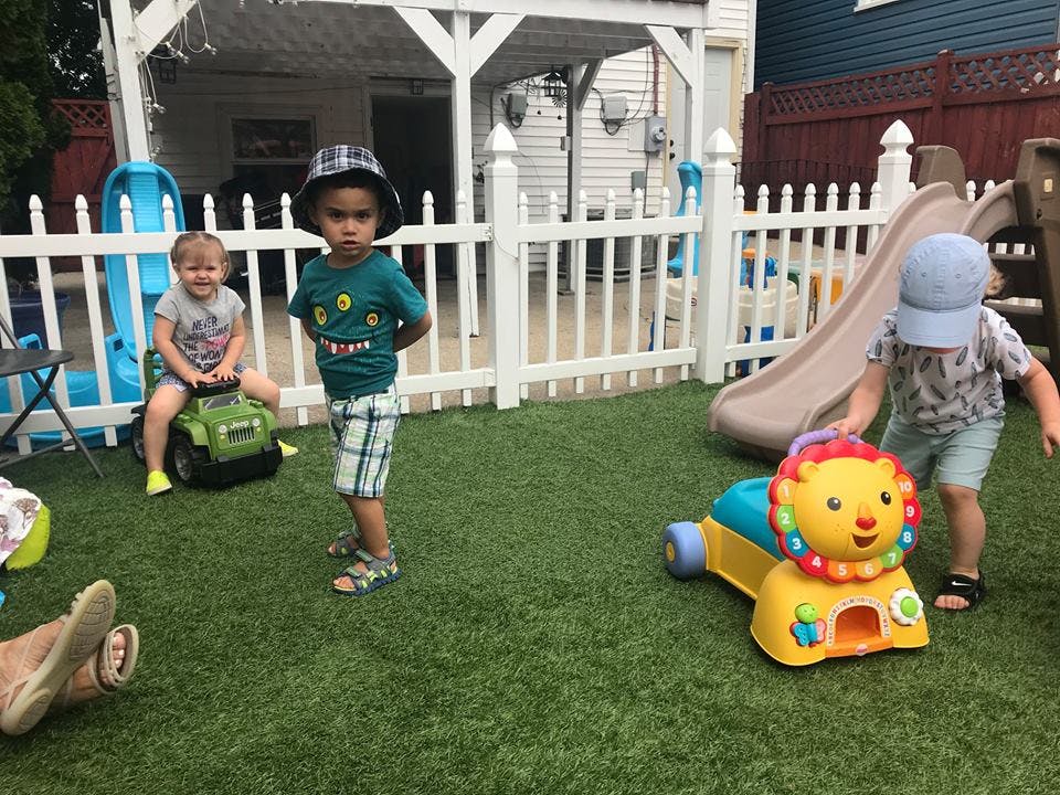 Three children playing with toys in a fenced yard
