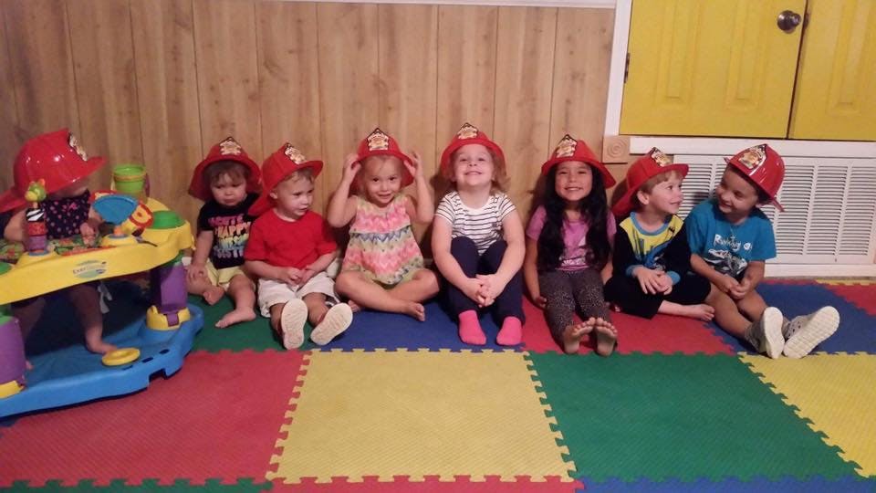 Children wearing firefighter hats sitting on a colorful mat
