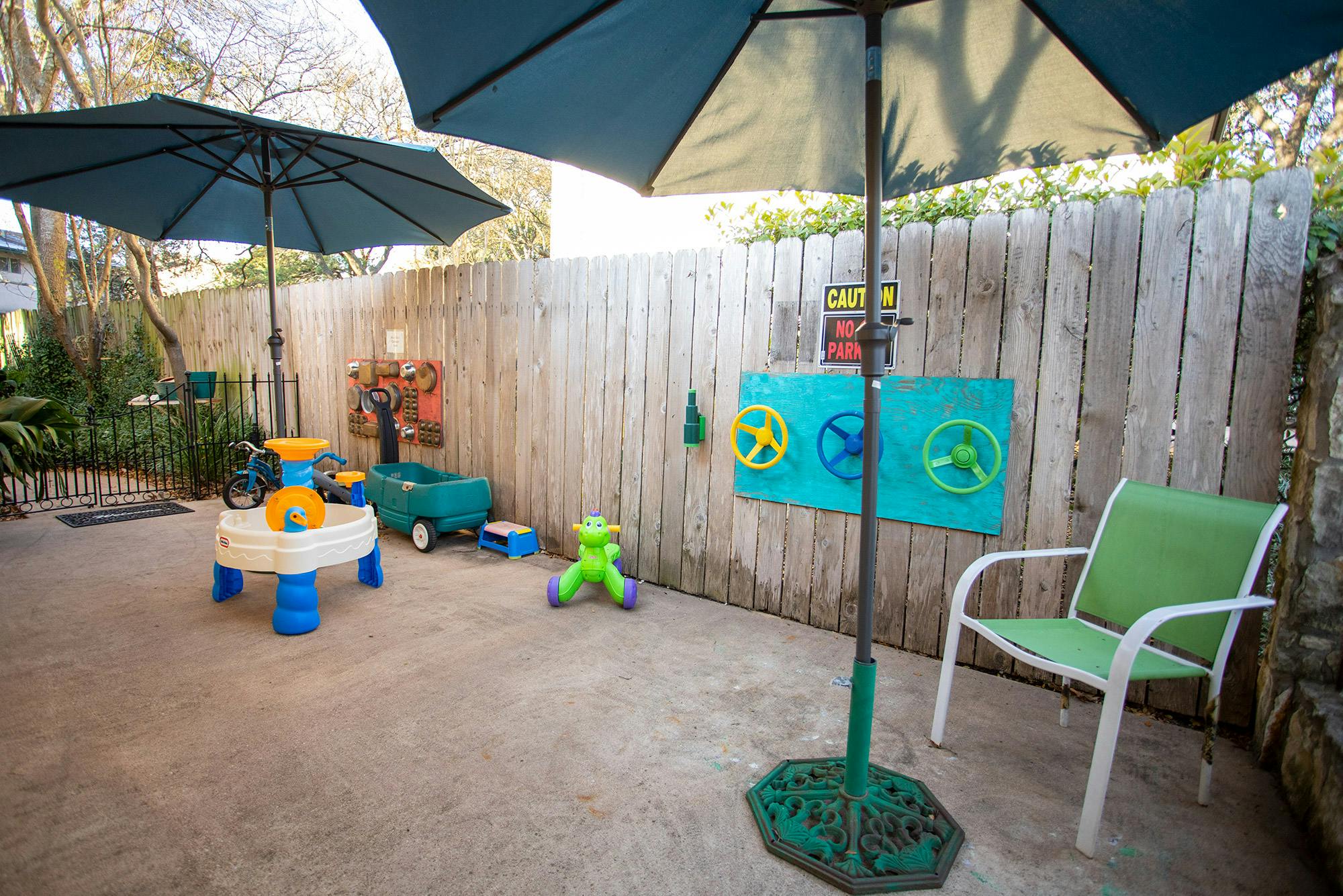 Outdoor patio with umbrellas, children's play table, wagon, and green chair