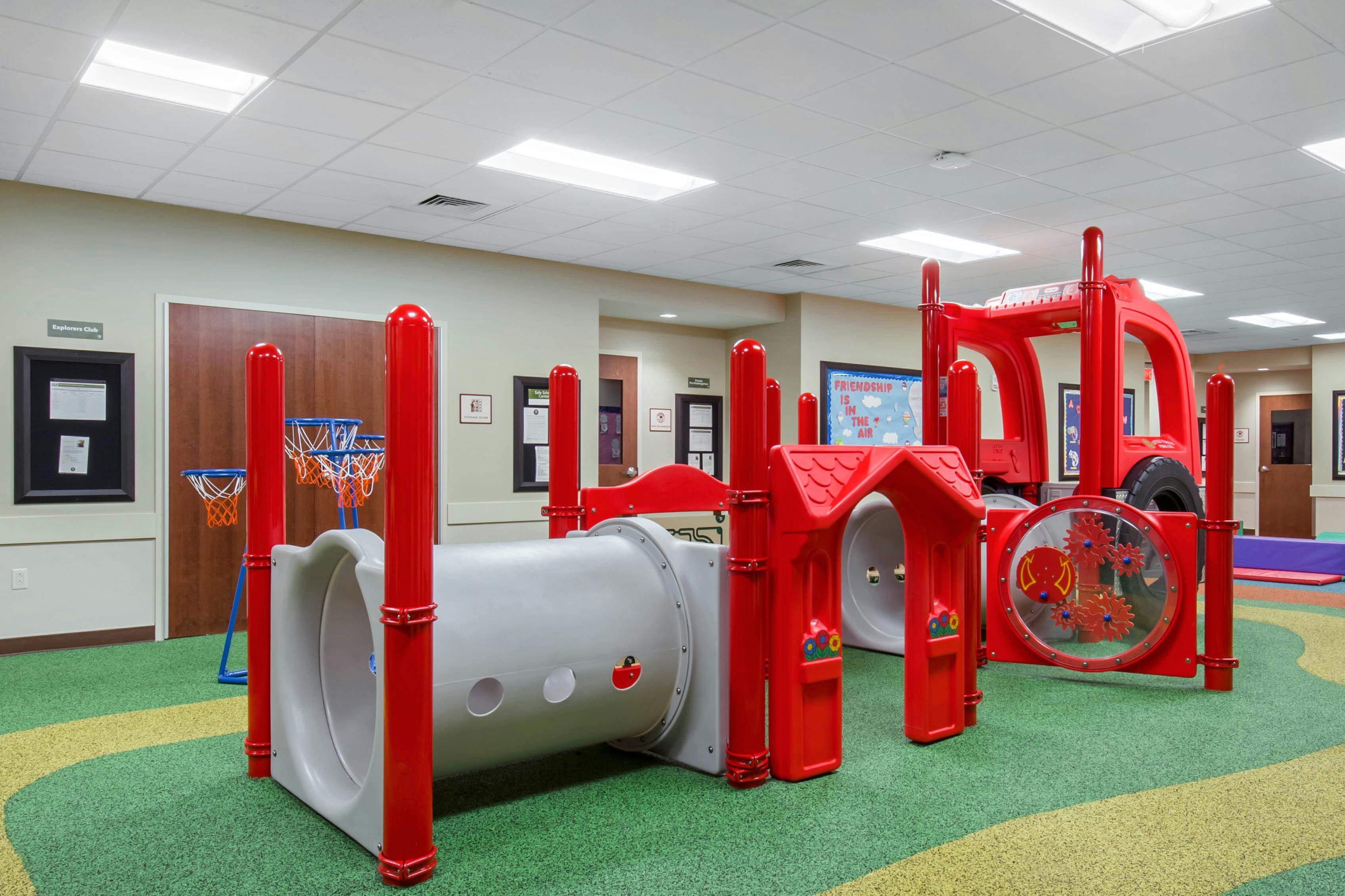 Indoor playground with red and gray play equipment and multiple basketball hoops