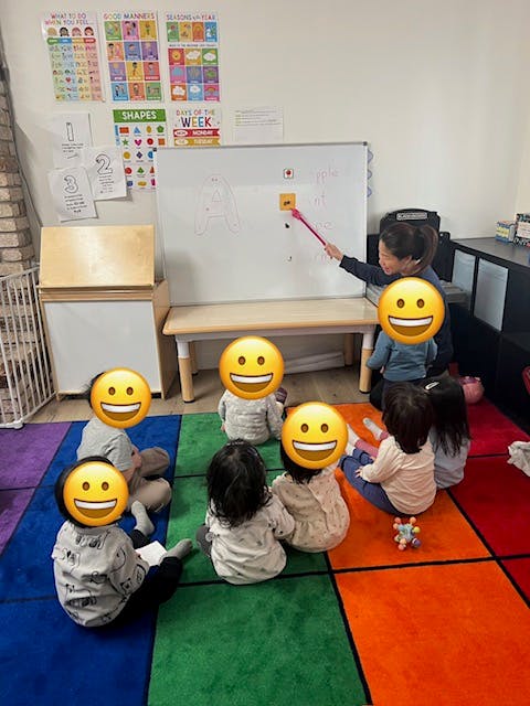 Person pointing at a whiteboard with children sitting on the floor