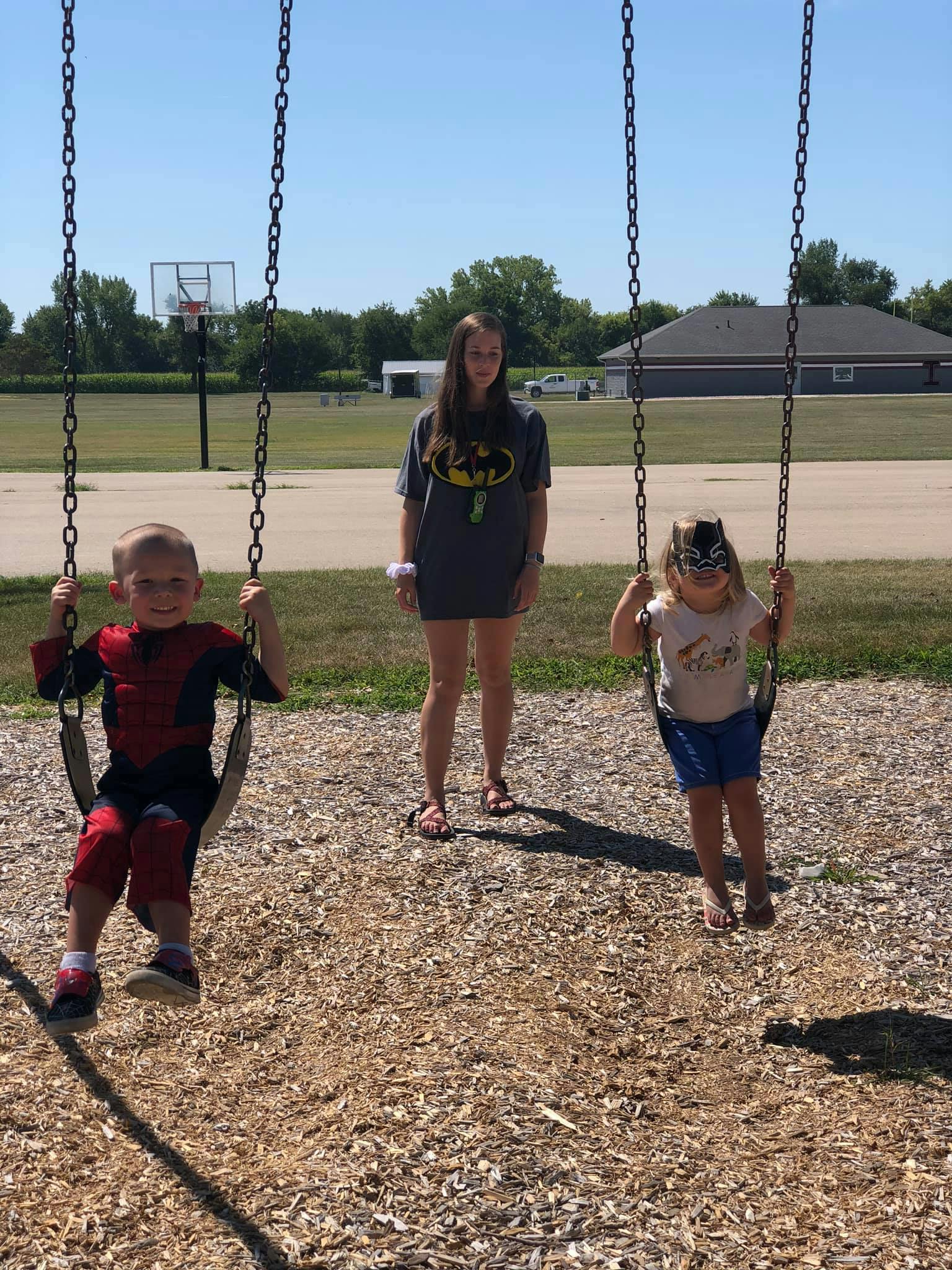 Two children on swings and a teen standing between them on a playground