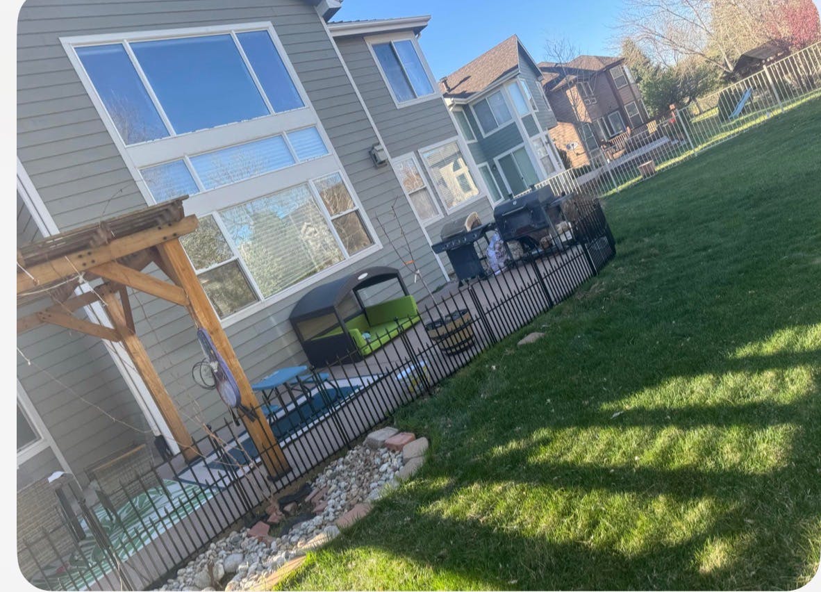 Backyard patio with a metal fence, wooden pergola, and grill next to a house