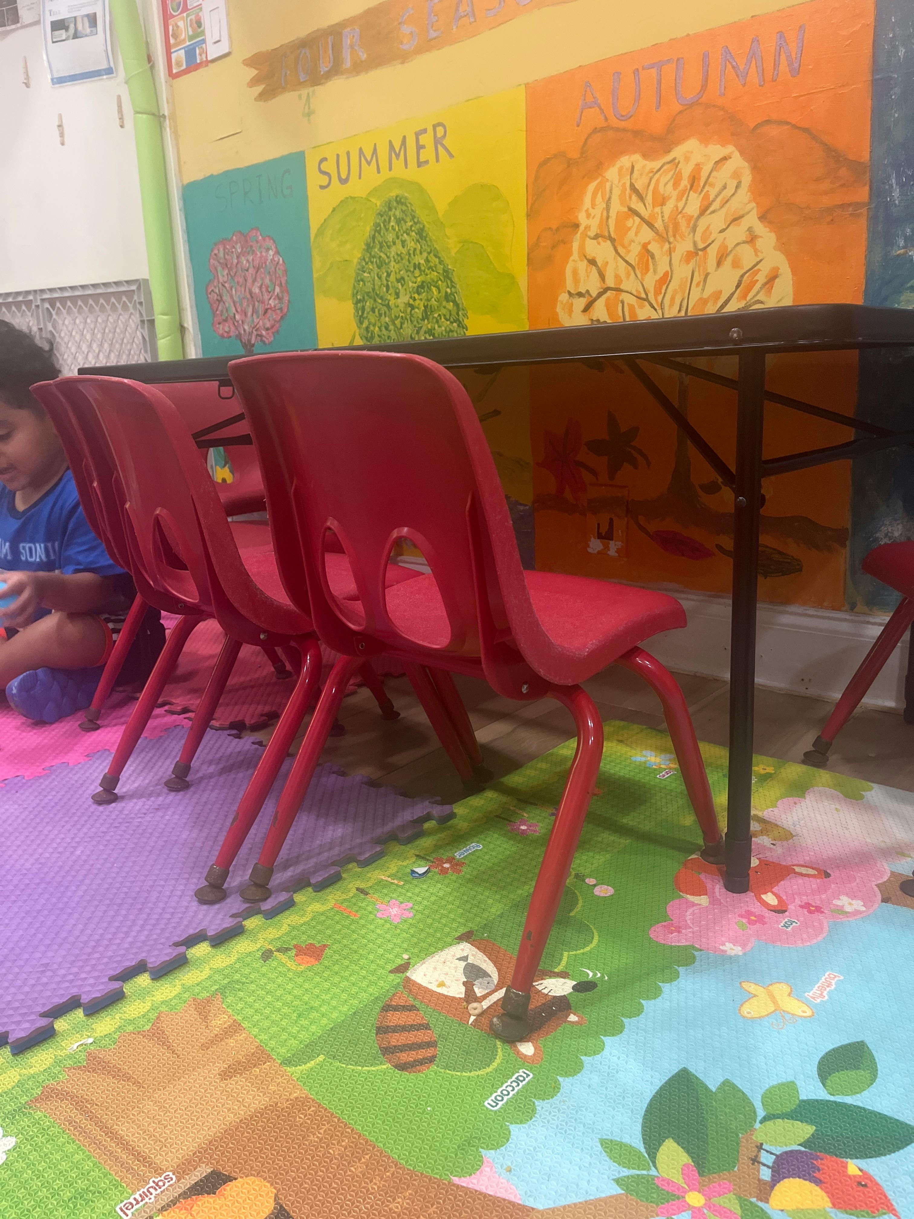 Child sitting on a play mat beneath a table with red chairs