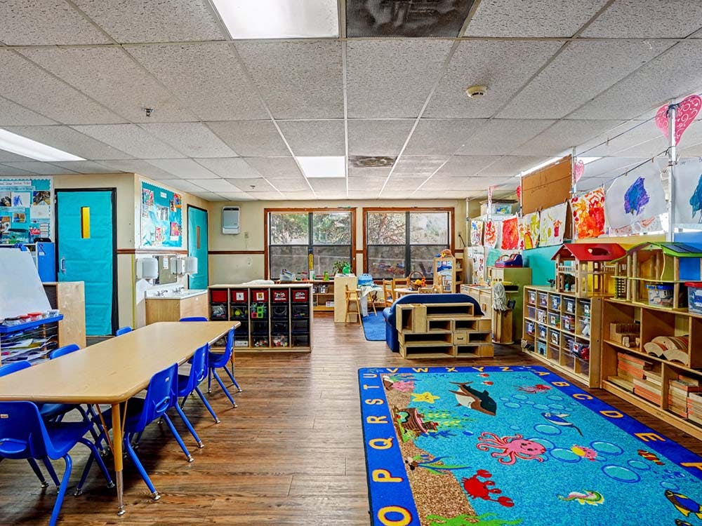 Classroom with tables, chairs, sinks, and a colorful rug