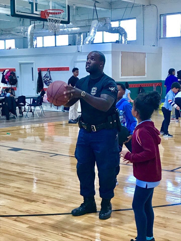 Person in uniform holding a basketball with a child in a gymnasium