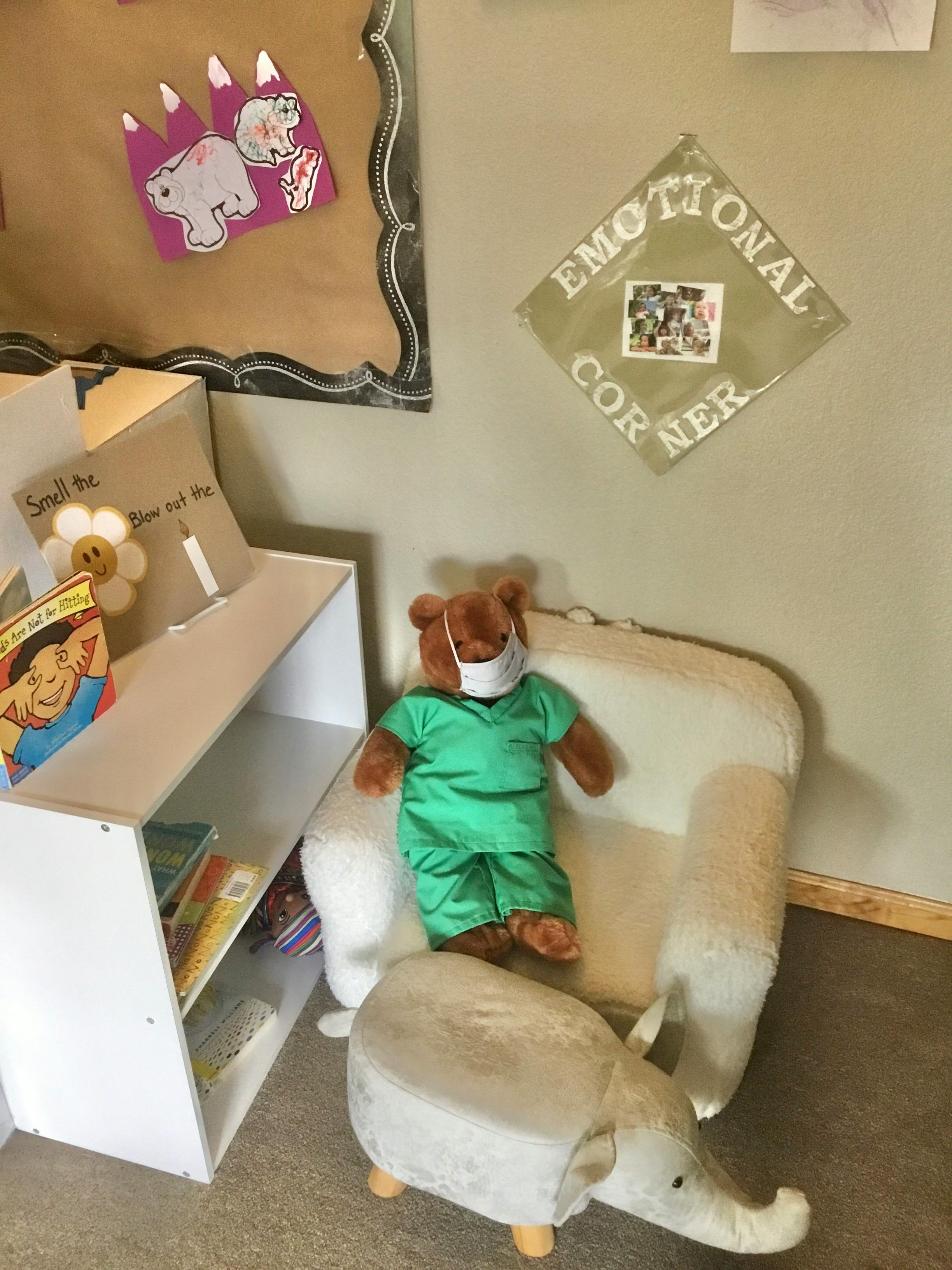 Teddy bear in scrubs and face mask sitting in a chair next to a bookshelf