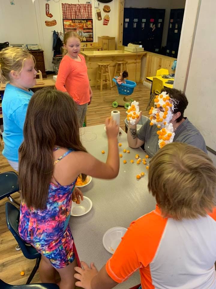 Children and an adult playing a game with whipped cream and cheese puffs