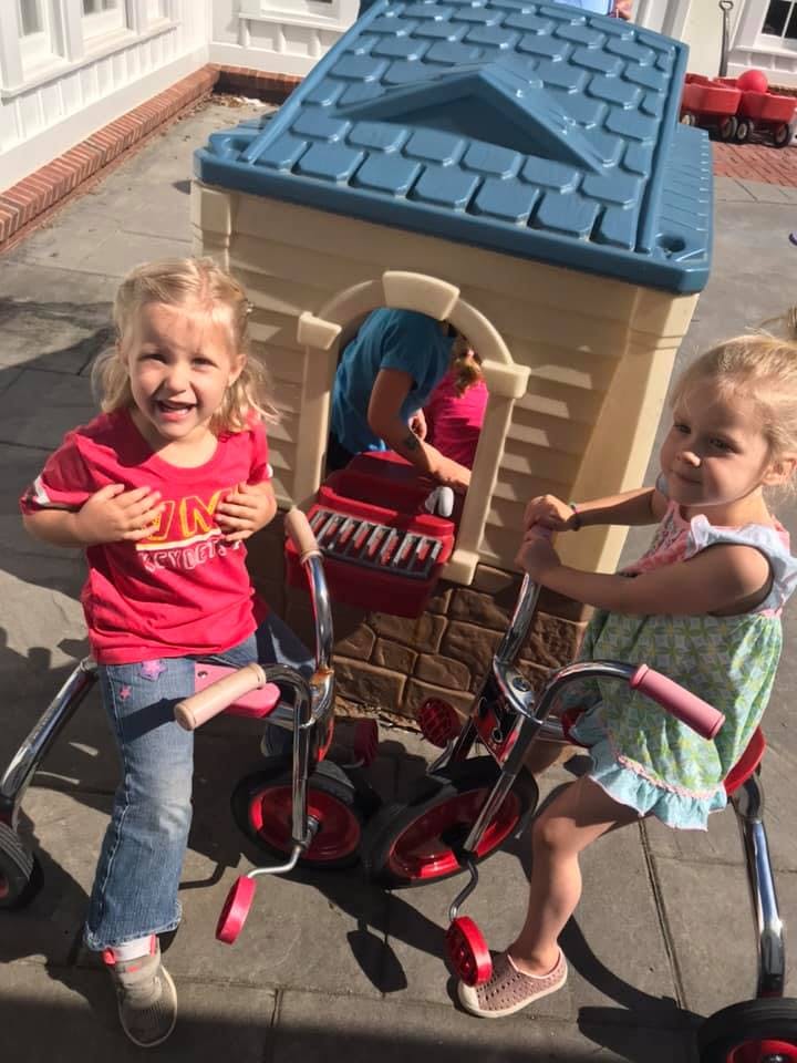 Two children on tricycles next to a playhouse
