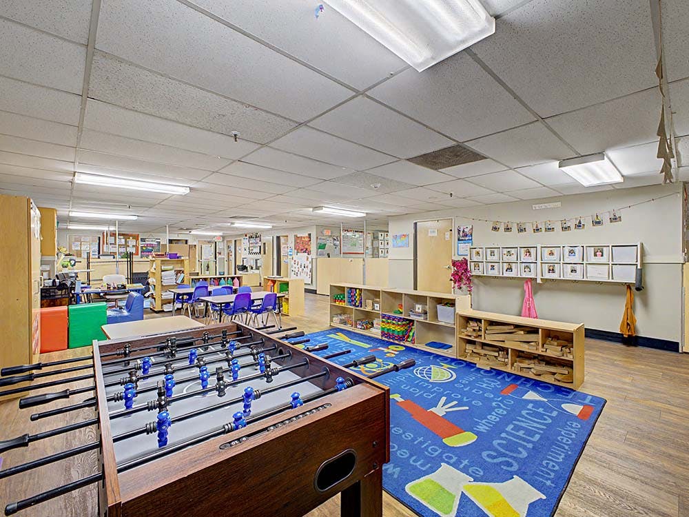 Classroom with a foosball table, small blue chairs, and a science-themed rug