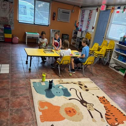 Four children sitting at a yellow table in a classroom