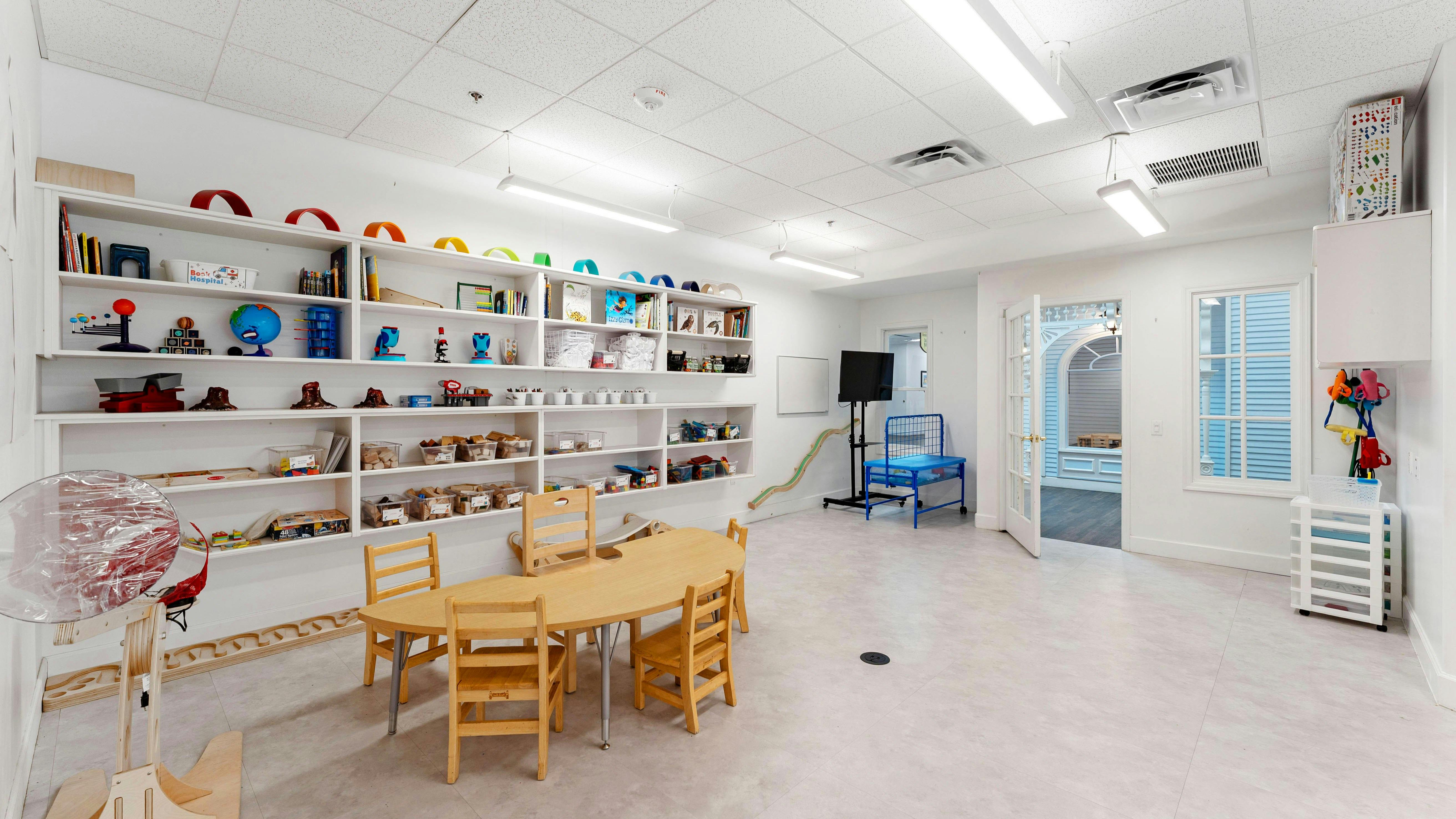 Classroom with shelves of colorful toys and books, a kid-sized table with chairs