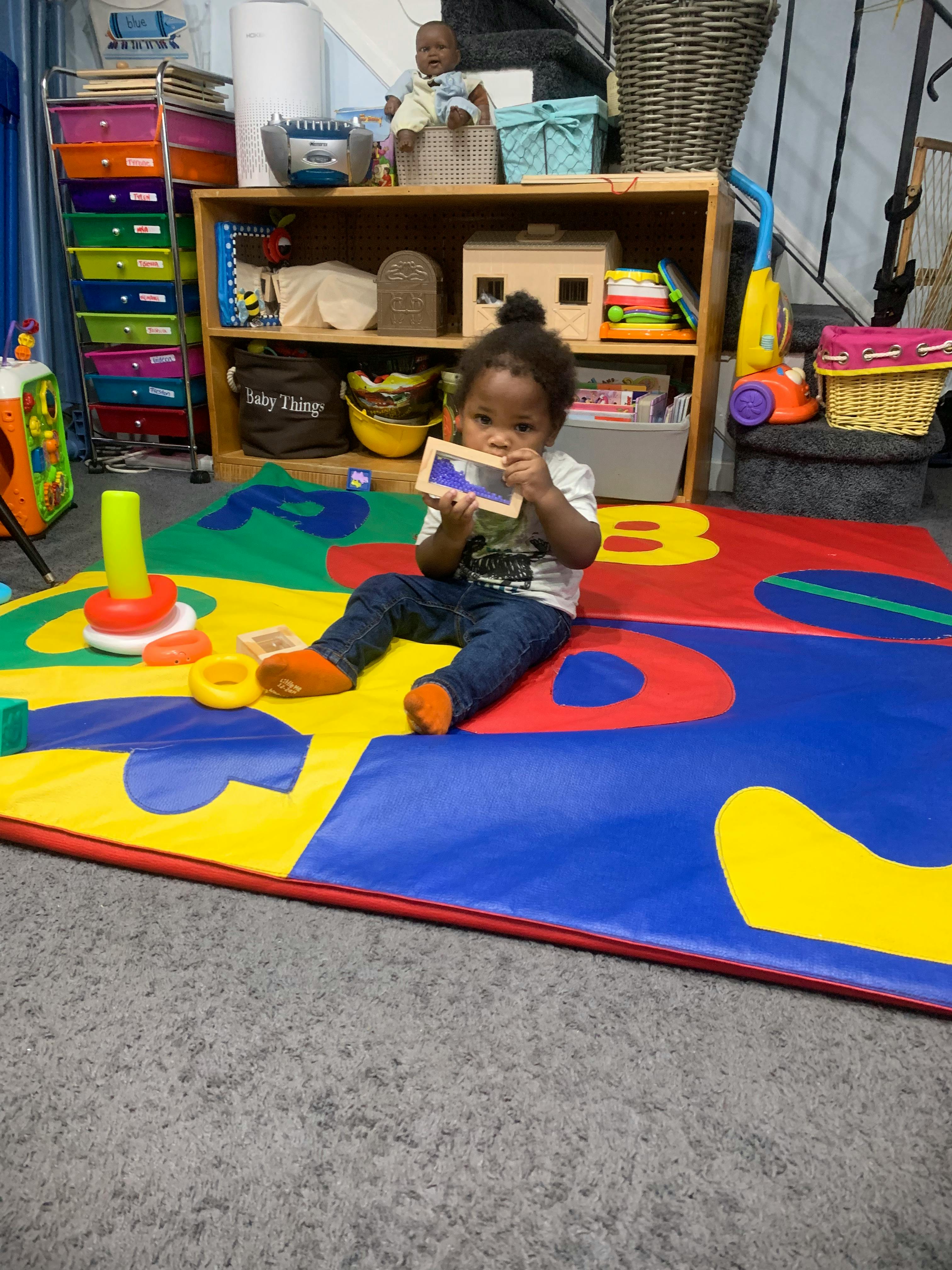 Child sitting on a colorful playmat holding a small mirror