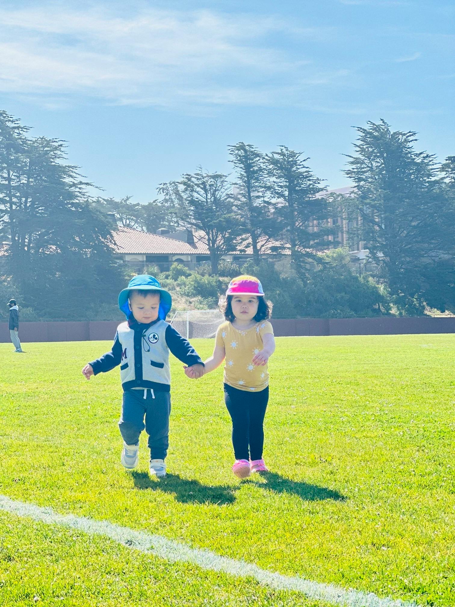 Two children holding hands and walking on a grassy field