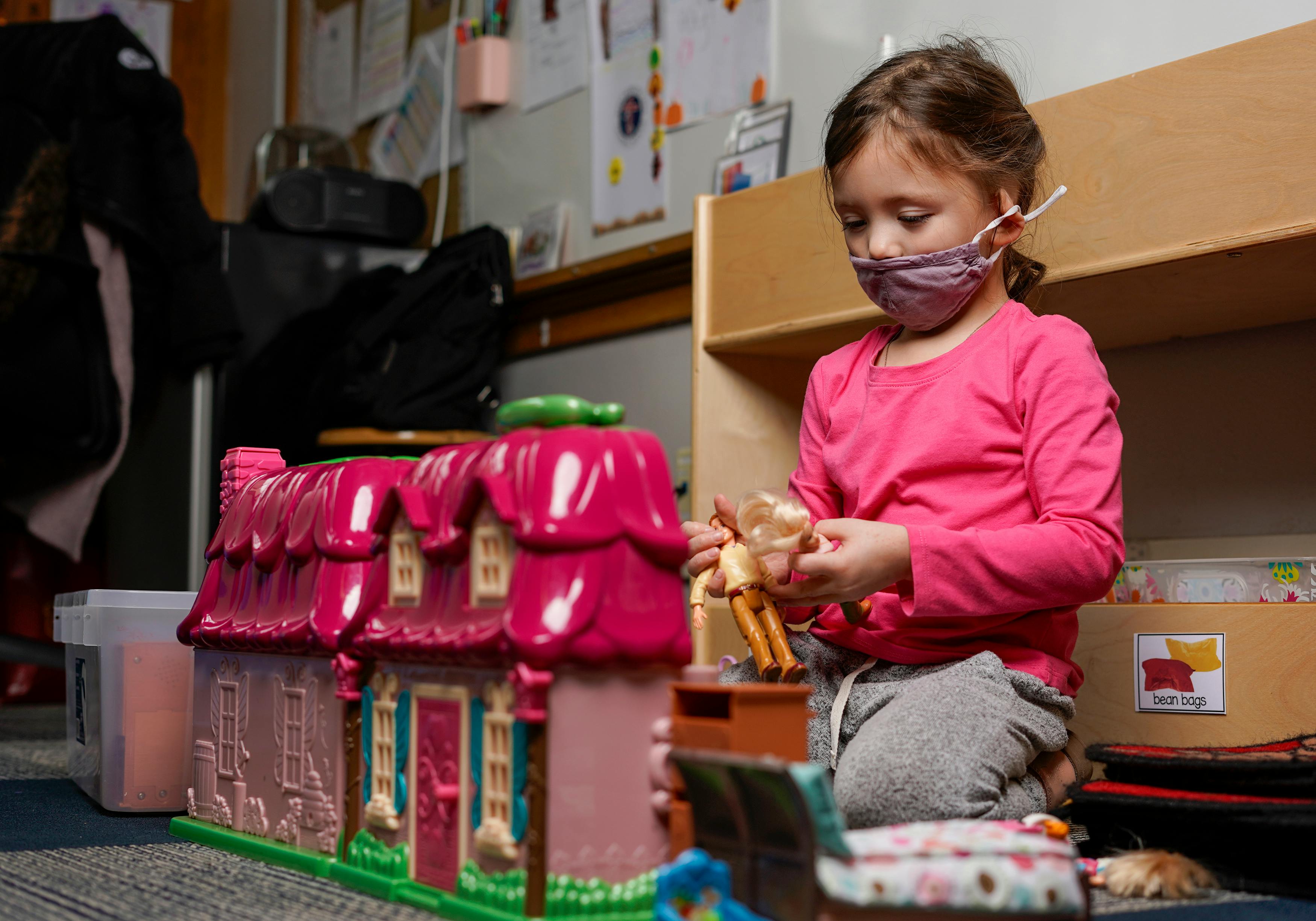 Child in a mask playing with a dollhouse and doll