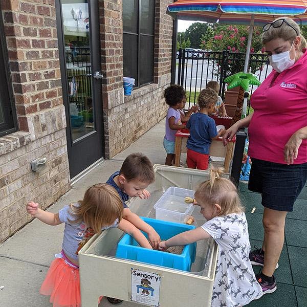 Adult and children playing at a sensory table outdoors
