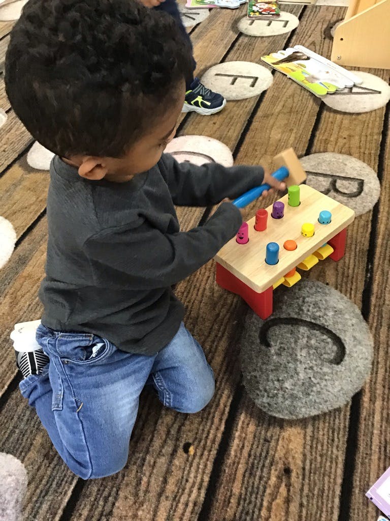 Child kneeling on floor playing with a wooden pounding toy