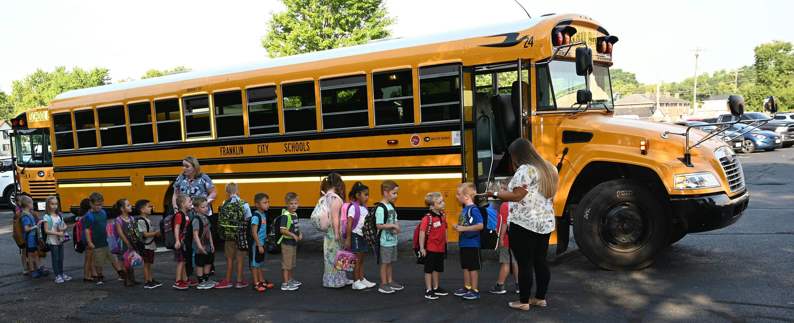 Children and an adult standing in line next to a school bus