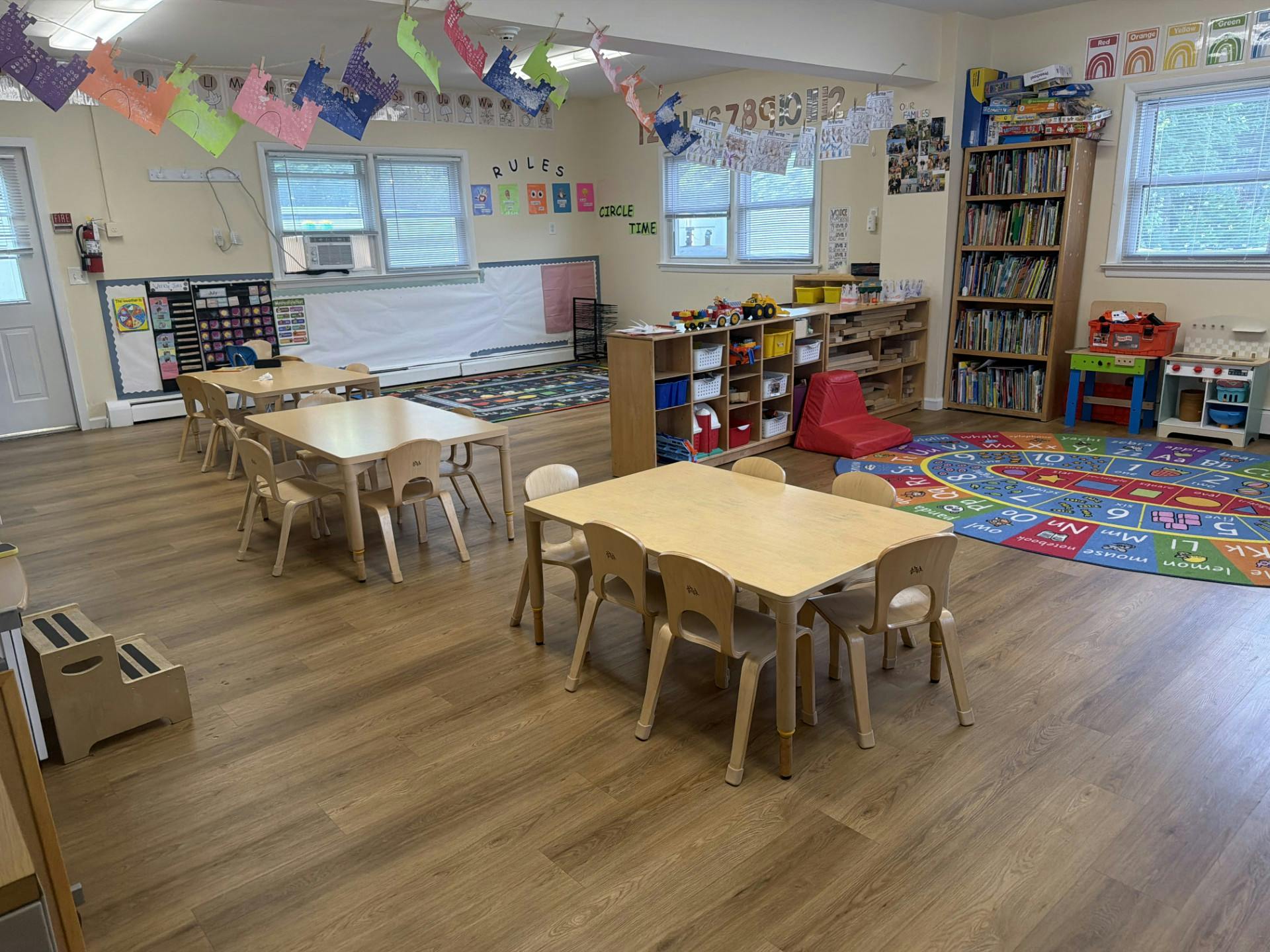 Empty preschool classroom with wooden tables, chairs, and learning stations