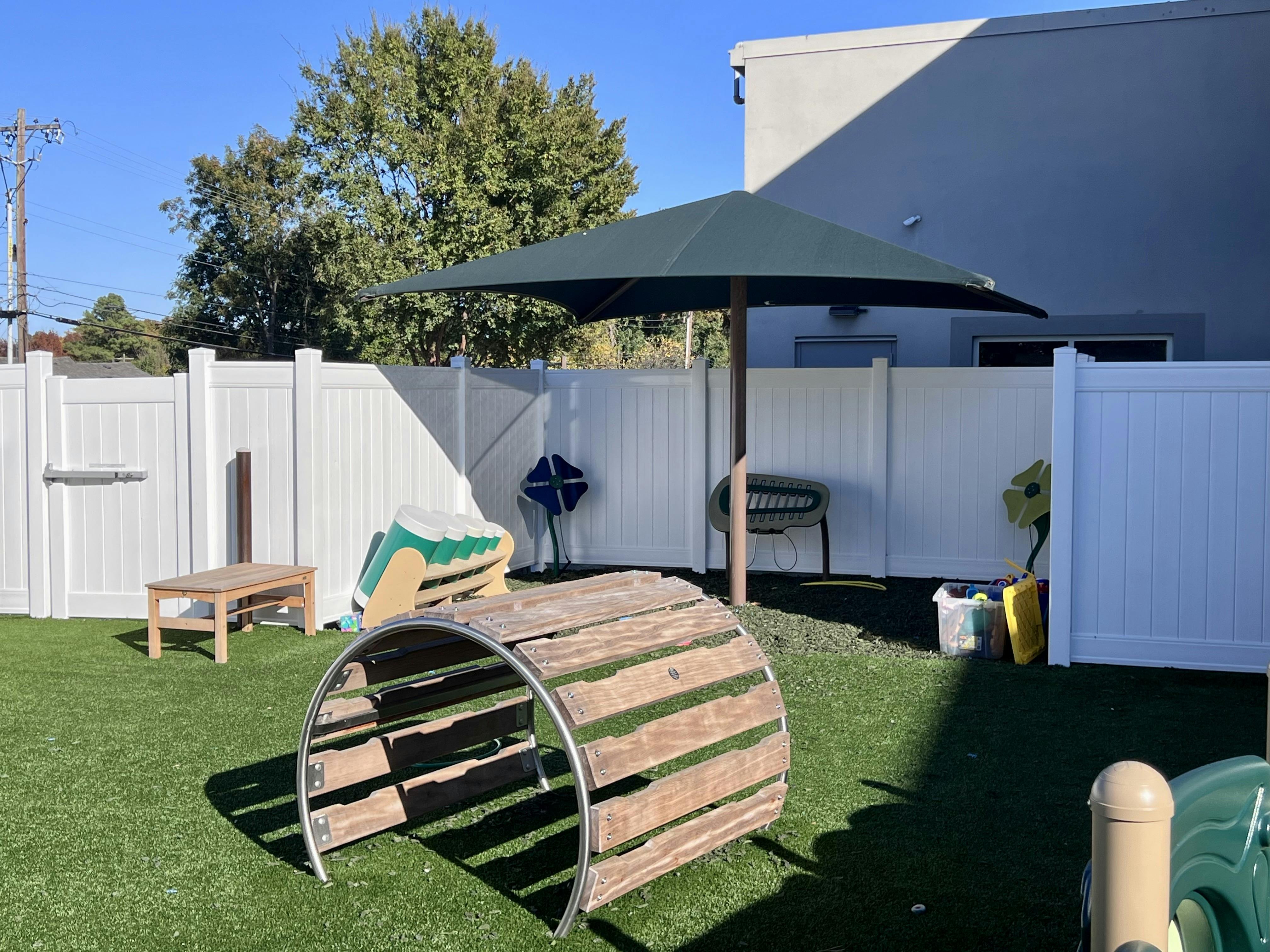 Outdoor play area with a wooden tunnel, green umbrella, and white fence