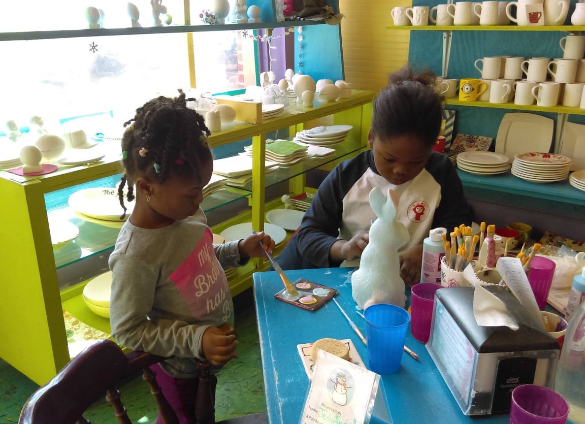 Two children painting ceramic figures at a table