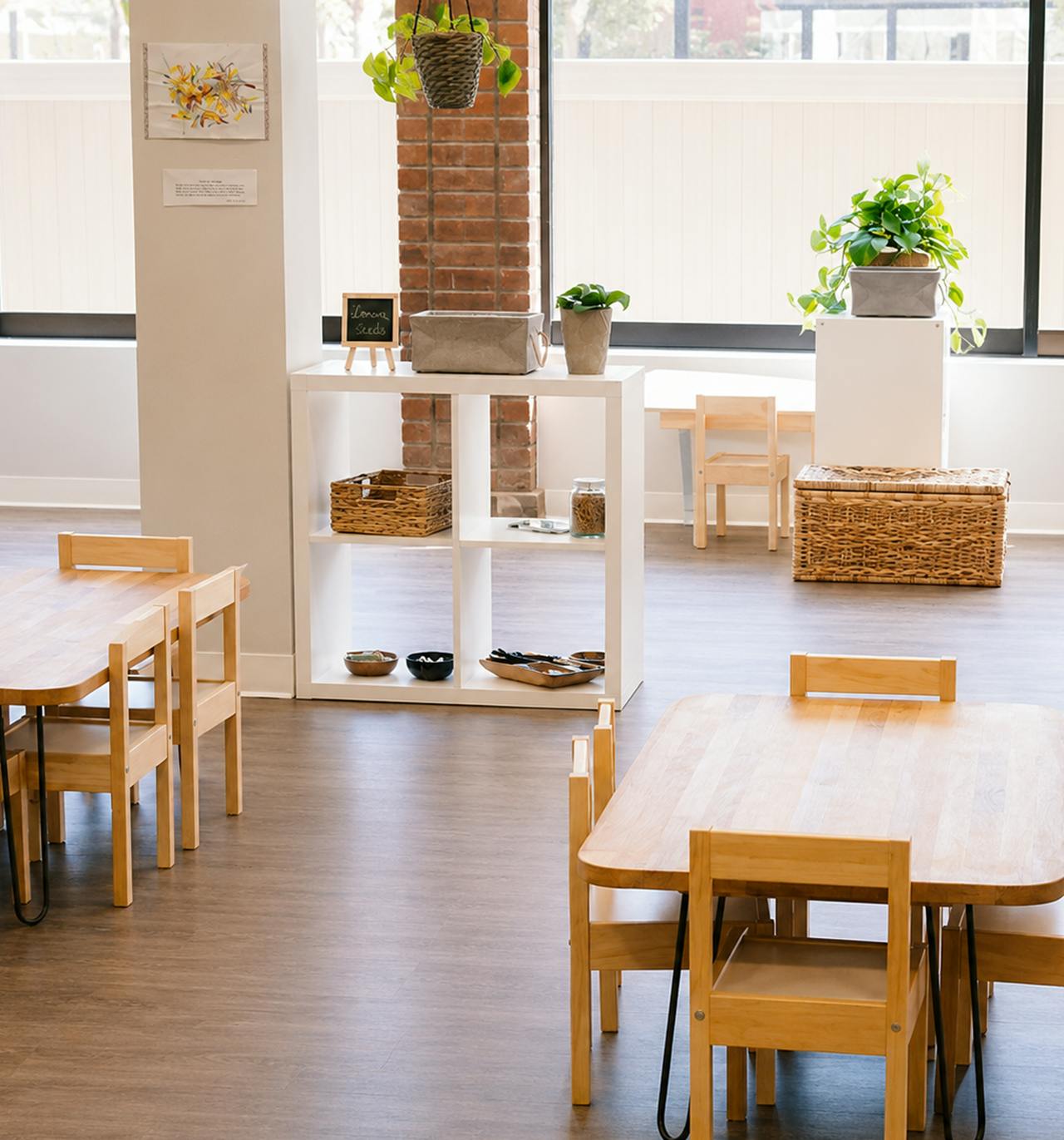 Children's tables and chairs in a classroom with wooden shelving and plants