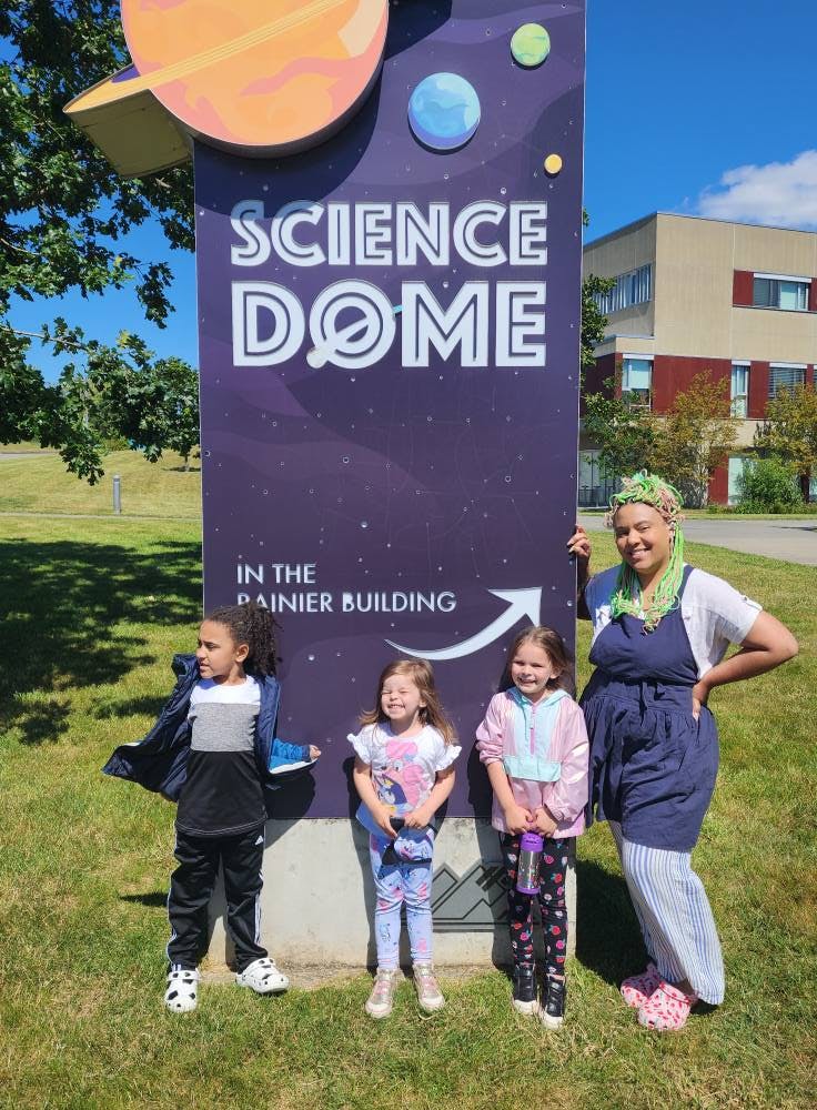 A person and three children standing by a Science Dome sign