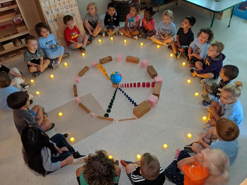 Children sitting in a circle around a spiral of blocks and small lights
