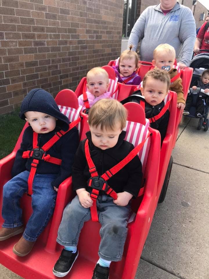 Multiple children in a red multi-seat stroller being pushed by a person