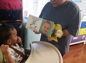 Person holding a book for a child in a high chair
